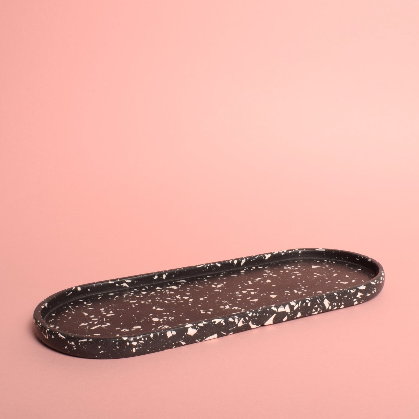 A large oval black trinket tray with white terrazzo chips in it.